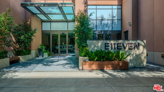 Front view of a modern building entrance with a glass canopy and plants.