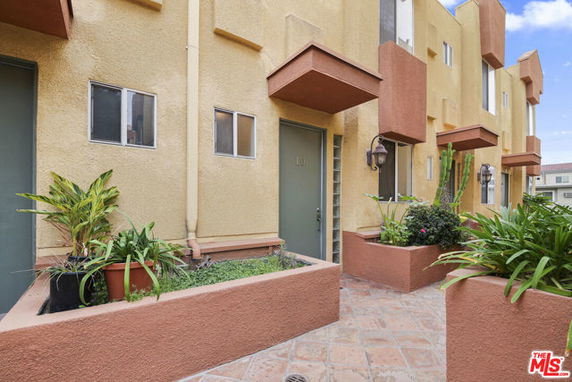 Front view of a multi-story building with small entryways and potted plants.