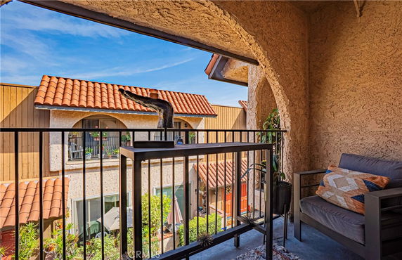 View from a balcony overlooking nearby building with arched windows and tile roof.