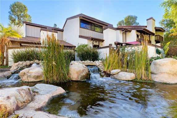 Front view of a multi-story house with stone accents and a small waterfall in the garden.