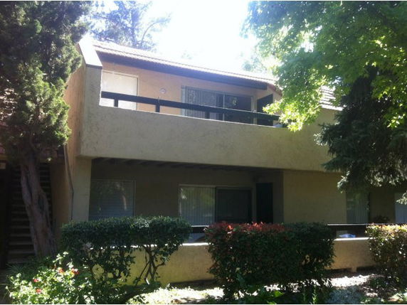 Front view of a two-story house with a balcony and surrounding greenery.