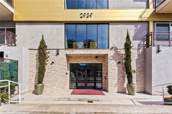 Front view of a modern building entrance with large windows and potted plants.