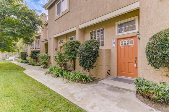 Front view of a two-story townhouse with an orange door and shrubs.