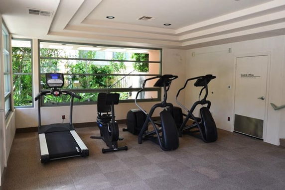 Room with exercise equipment, including a treadmill and elliptical machines.