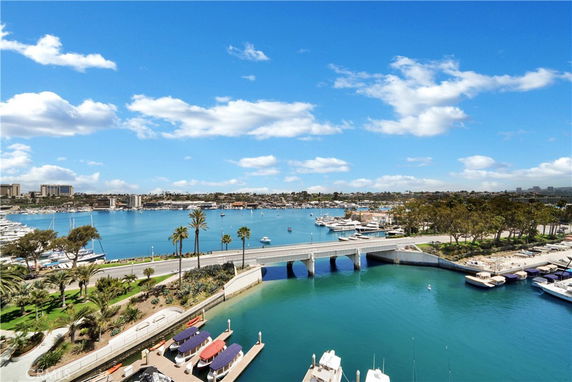 Panoramic view of a marina with boats and a bridge over blue water under a partly cloudy sky.