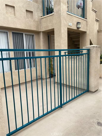 Front view of a multi-story beige building with teal railings and a small gated entrance.