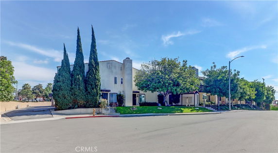 Front view of a residential building with trees and a sidewalk.
