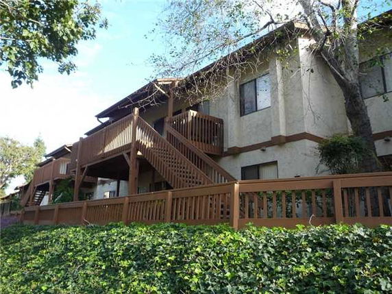 Side view of a two-story building with exterior stairs and a wooden fence.
