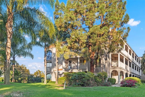 Front view of a multi-story building with balconies and arches, surrounded by trees.