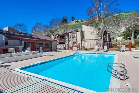 Outdoor swimming pool with a patio area and loungers, surrounded by buildings.