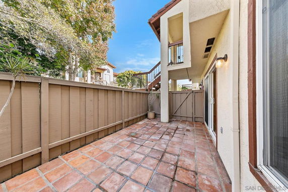 Outdoor patio view with tiled flooring, fenced area, and nearby trees.