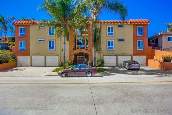Front view of a multi-story apartment building with garages and palm trees.