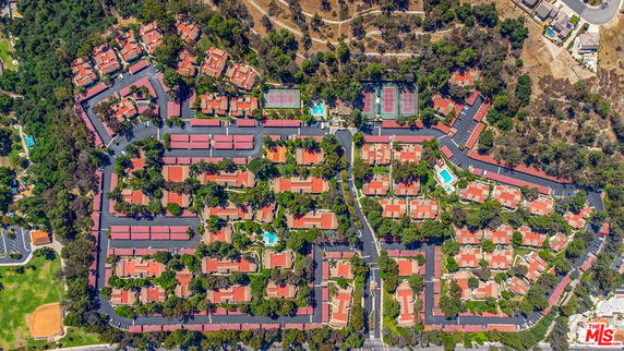 Aerial panoramic view of a residential area with multiple houses and tennis courts surrounded by trees.