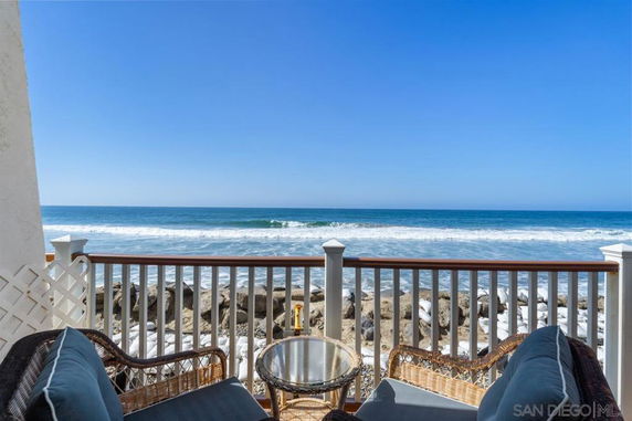 Wide angle view of ocean from a balcony with wicker chairs and a table.