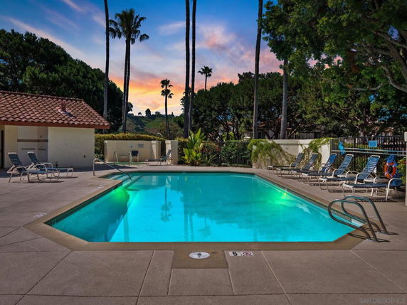 Outdoor swimming pool area with lounge chairs and trees in the background.
