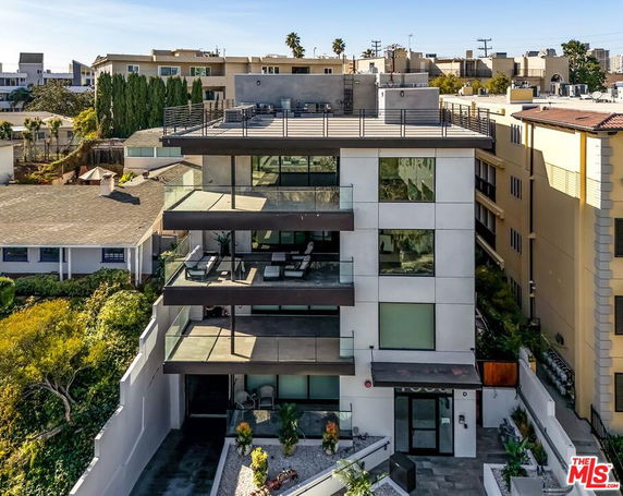 Front view of a modern multi-story building with glass balconies and a rooftop terrace.