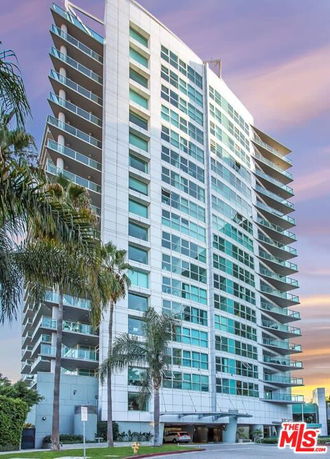 Front view of a tall residential building with multiple balconies and large windows.