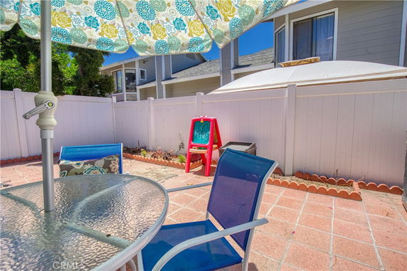 Outdoor seating area with a glass table, chairs, and a colorful umbrella adjacent to a house.