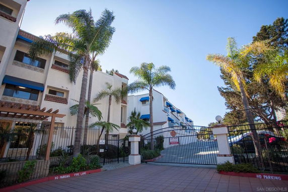 Front view of a multi-story building with palm trees and a gated entrance.