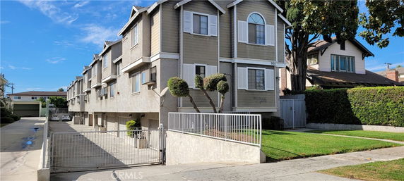 Front view of a multi-story residential building with gated entry and landscaped yard.