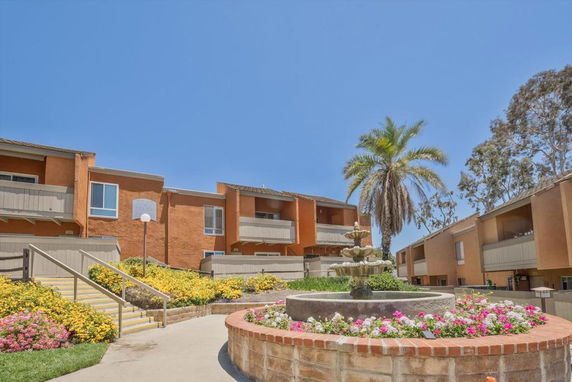 Front view of a multi-story apartment building with balconies and a central courtyard fountain.