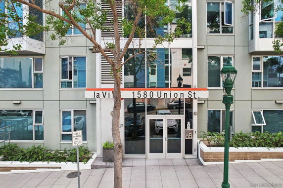 Front view of a multi-story residential building with glass entrance doors and multiple windows.