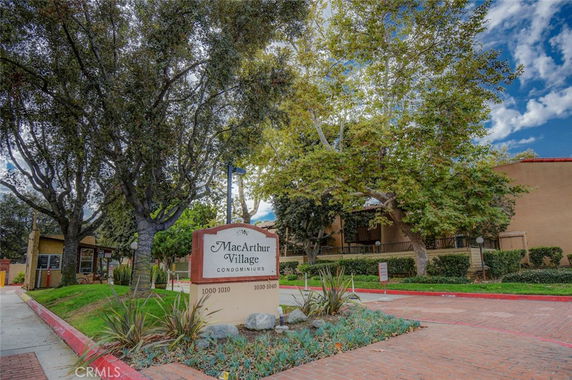 Front view of MacArthur Village Condominiums with trees and a sign at the entrance.