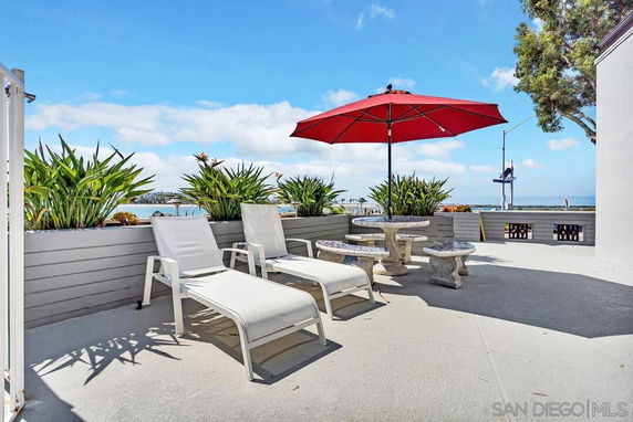 Outdoor seating area with lounge chairs and umbrella facing water view.