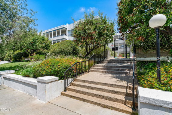 Front view of a multi-story building with stairs leading up surrounded by lush greenery.
