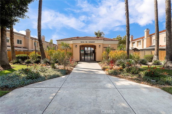 Front view of a gated residential entrance with a paved walkway and landscaped garden.