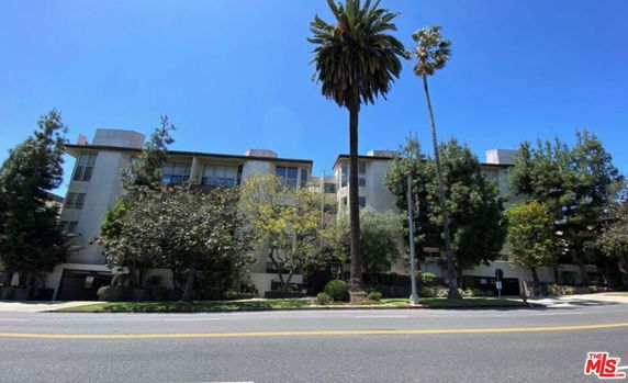 Front view of a multi-story apartment building with trees and a clear blue sky.