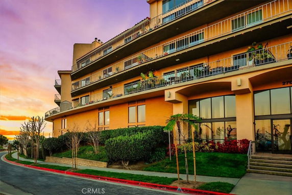 Front view of a multi-story building with balconies and large windows at sunset.