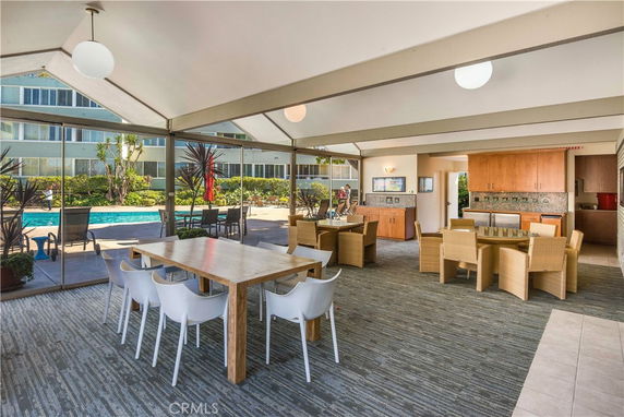 Interior view of a clubhouse with tables and chairs, overlooking a swimming pool.