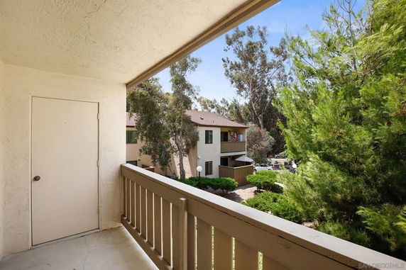 Outdoor view from a balcony showing a neighboring building and trees.