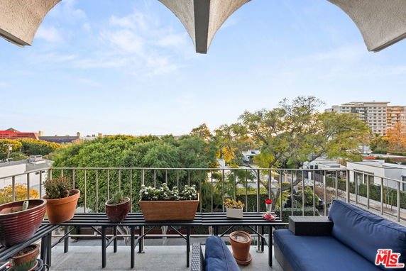 View from a patio with plants and outdoor seating overlooking surrounding buildings and trees.