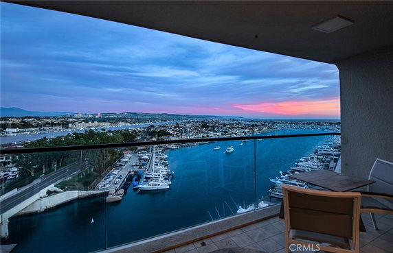 Panoramic view from a balcony overlooking a marina with boats docked and a distant city skyline at sunset.