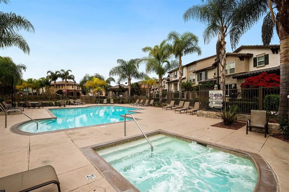 Outdoor swimming pool and jacuzzi area with surrounding lounge chairs and palm trees.