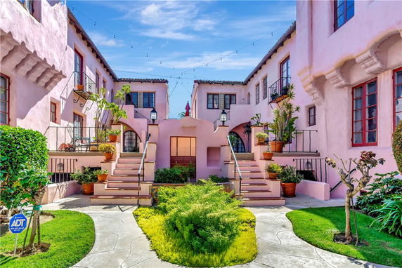 Front view of a pink two-story building with balconies and ornamental plants.