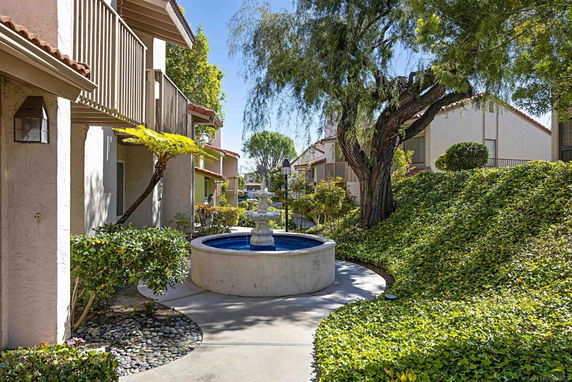 View of a landscaped courtyard with a central fountain, surrounded by residential buildings and trees.