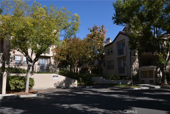 Front view of a residential building with trees and a shaded area.