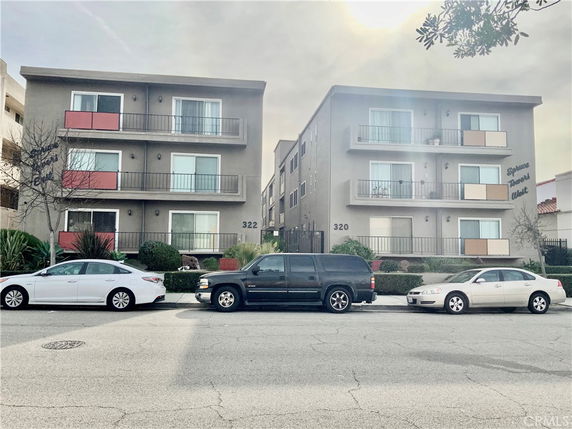 Front view of a three-story apartment building with balcony railings and parked cars in front.