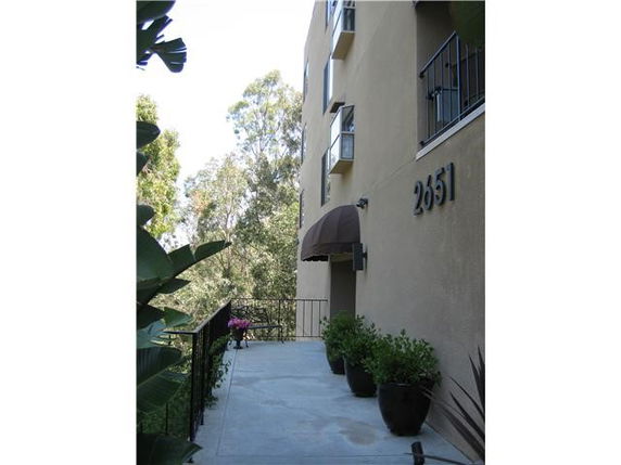 Side view of a multi-story building with plants along a walkway.