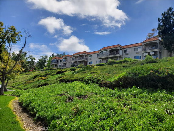 Front view of apartment buildings on a sloped landscape with balconies and red-tiled roofs.