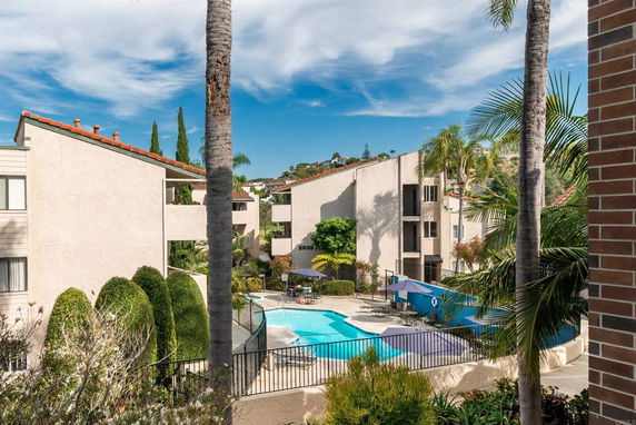 View of a residential building complex with a swimming pool surrounded by trees.