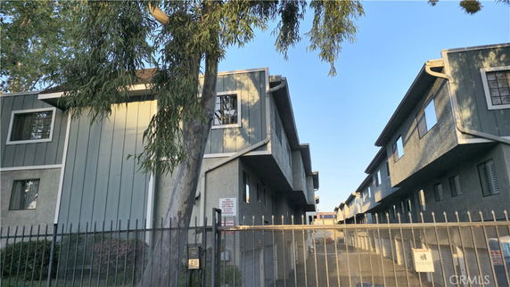 Front view of a multi-story apartment building with a gate and surrounding trees.