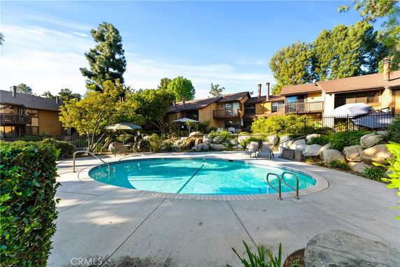 View of a residential complex with a circular swimming pool surrounded by greenery and outdoor seating.