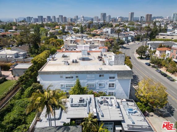 Aerial view of a building rooftop with air conditioning units and other equipment, surrounded by other residential buildings.