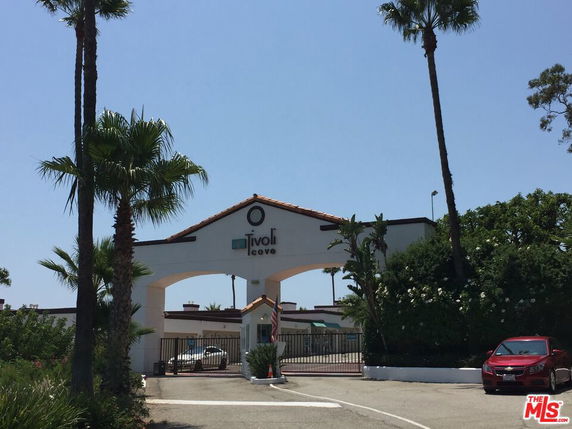 Front view of an entrance archway with a sign, flanked by palm trees.