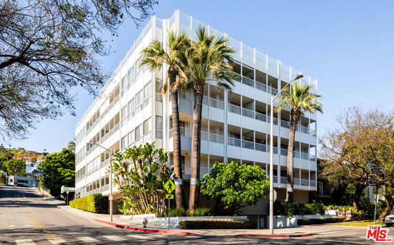 Front view of a multi-story apartment building with balconies and palm trees.