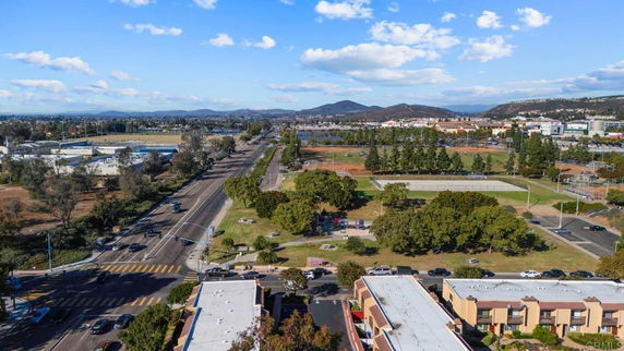 Aerial view of a road and surrounding areas with buildings, fields, and hills.
